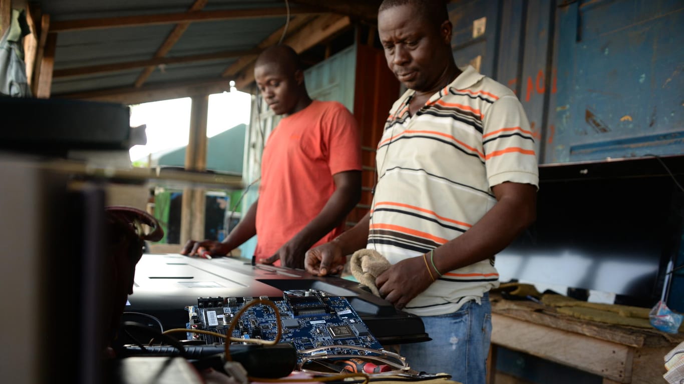 Tony Obour (rechts) repariert einen Fernseher in seiner Werkstatt in Accra, während ihm sein Lehrling über die Schulter schaut.