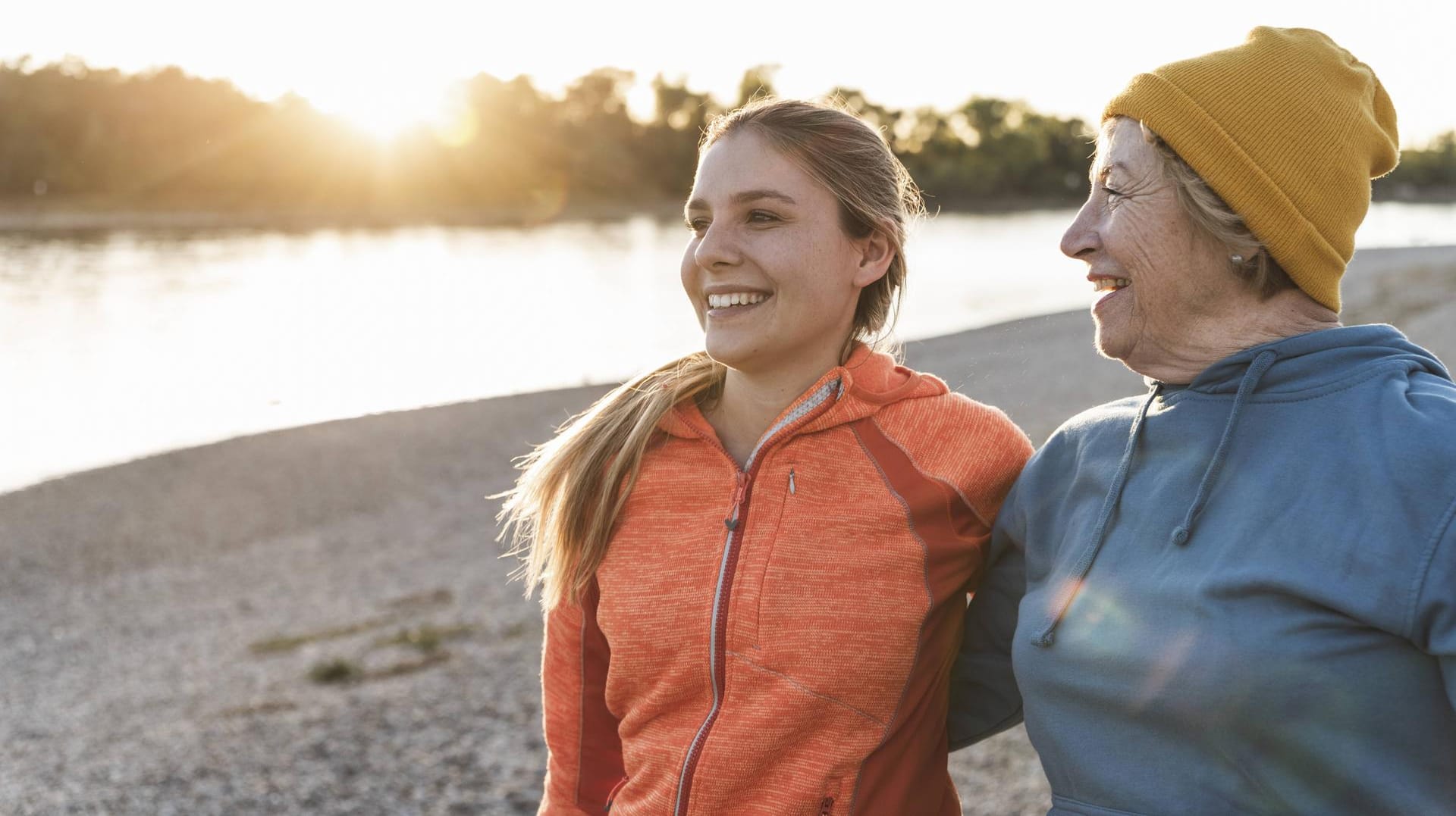 Fit grandmother and granddaughter walking at the river with arms around having fun model released S