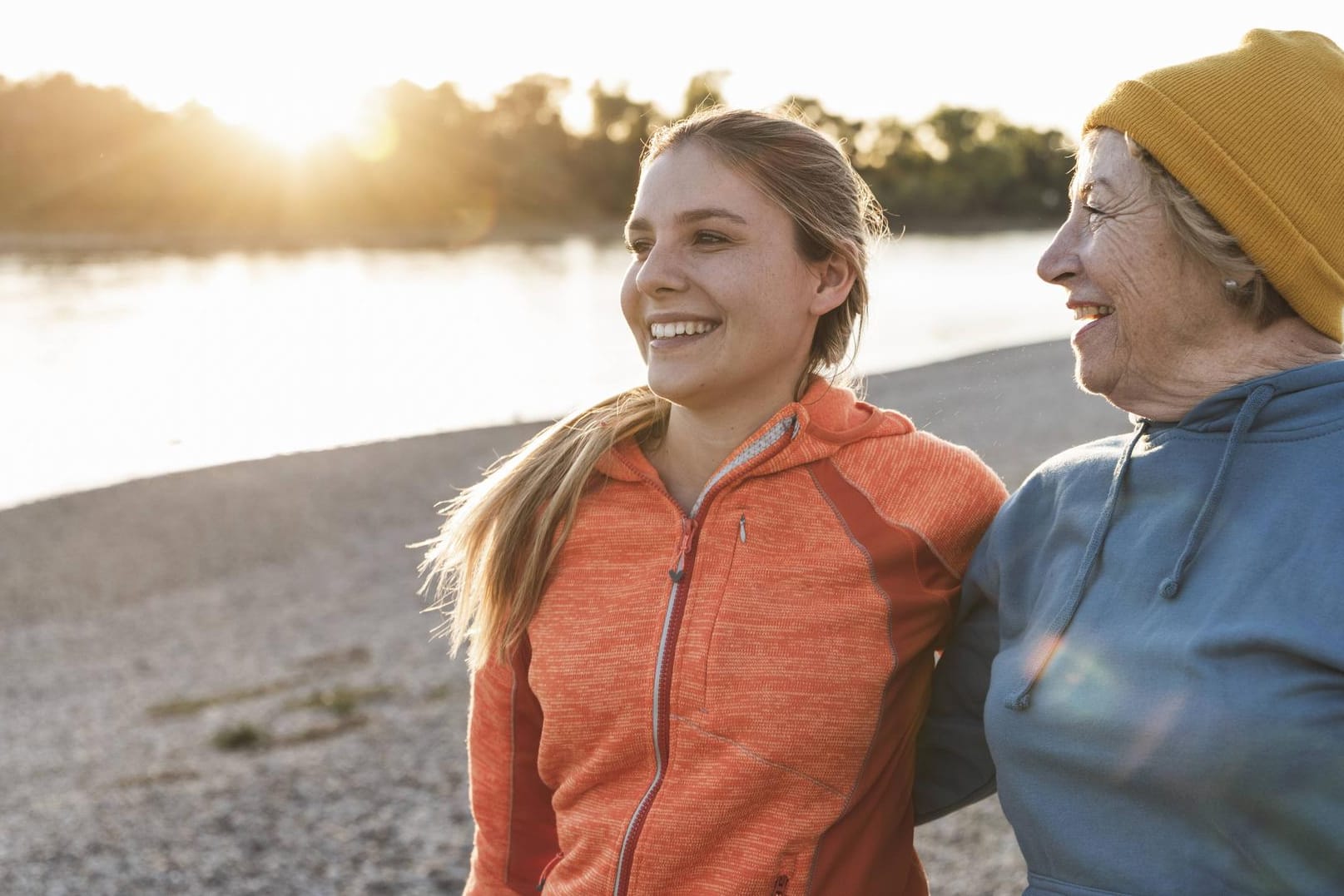 Fit grandmother and granddaughter walking at the river with arms around having fun model released S