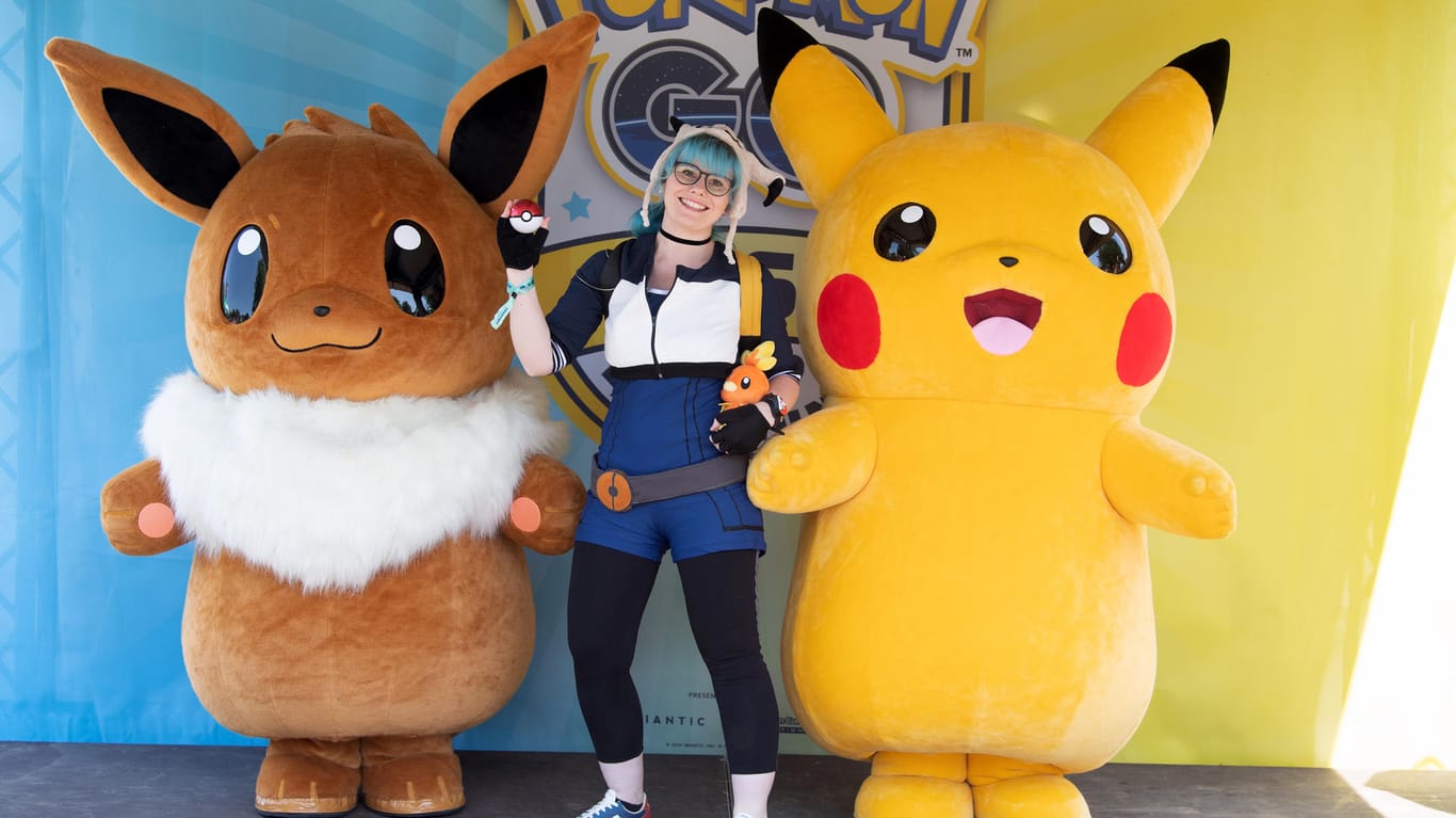 Eine Spielerin (M) posiert mit den Pokémon-Figuren Pikachu (r) und Eevee (l).