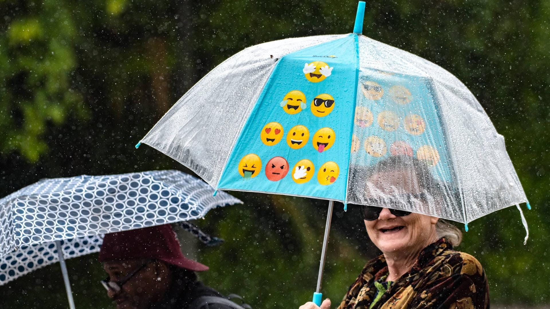 Eine Frau trägt einen Regenschirm mit Emojis drauf.