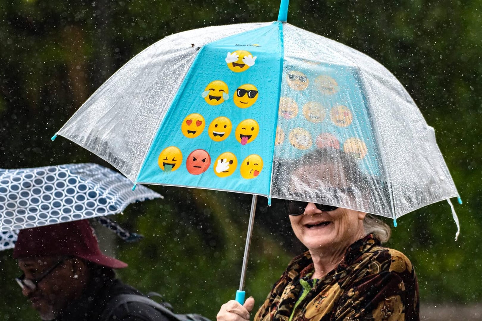 Eine Frau trägt einen Regenschirm mit Emojis drauf.