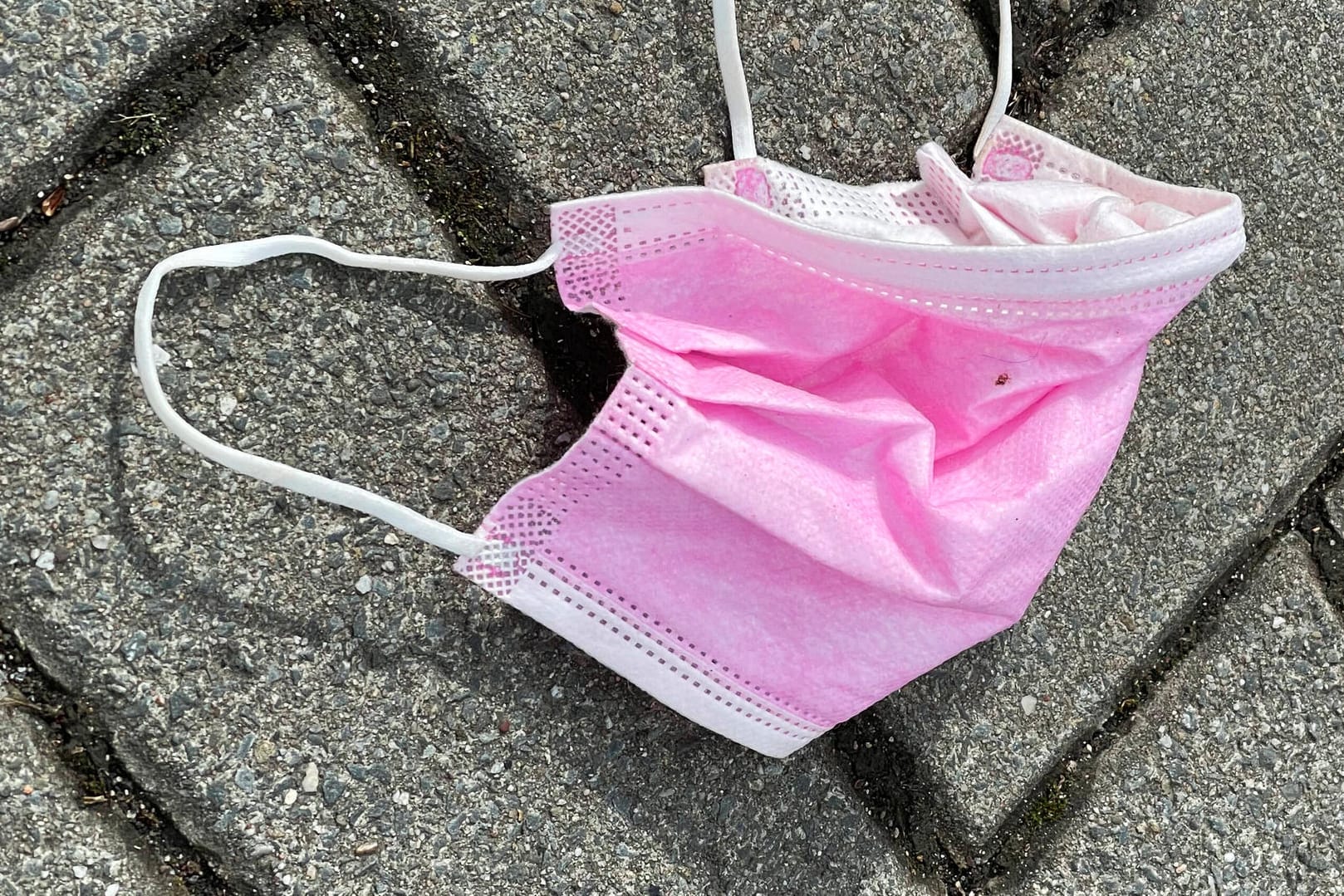 Symbolfoto pinke Gesichtsmaske auf Strassenbelag Symbolbild einer benutzten und entorgten medizinischen Maske und Mund N
