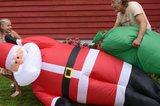 Lachend tragen Alicia und ihr Opa Dietmar Sawatzke den drei Meter großen aufgeblasenen Weihnachtsmann neben die mit Sommerblumen dekorierte Eingangstür.