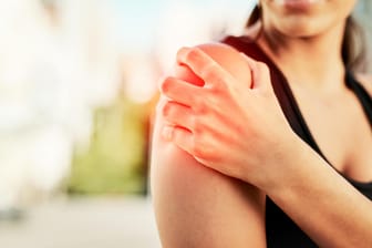 Eine Frau greift sich an die Schulter: Verspannungen im Schulterbereich können die Beweglichkeit stark einschränken. In vielen Fällen helfen regelmäßige Trainingsübungen.