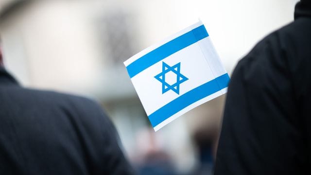 Bei einer Solidaritätskundgebung vor einer Synagoge hält ein Teilnehmer eine israelische Flagge in der Hand. Bei einer Solidaritätskundgebung vor einer Synagoge hält ein Teilnehmer eine israelische Flagge in der Hand.