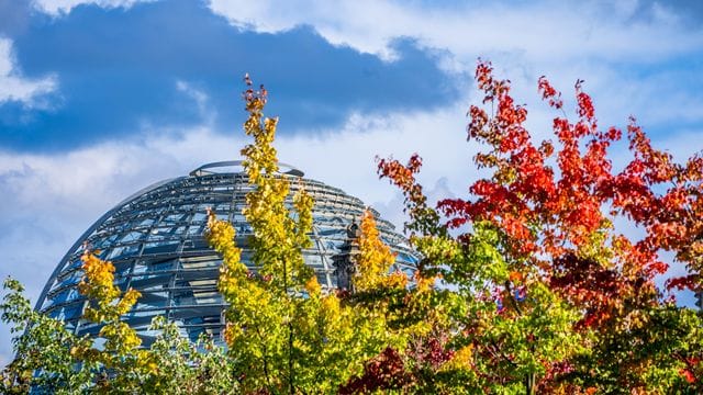 Die Kuppel auf dem Deutschen Bundestag hinter bunt gefärbten Laubbäumen. Die Kuppel auf dem Deutschen Bundestag hinter bunt gefärbten Laubbäumen.