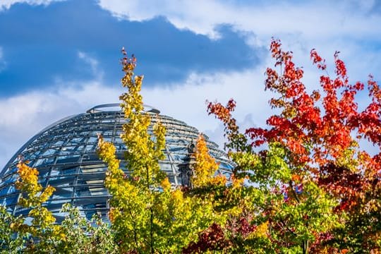 Die Kuppel auf dem Deutschen Bundestag hinter bunt gefärbten Laubbäumen.