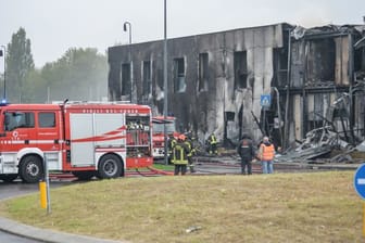 Feuerwehrleute stehen an der Unfallstelle, nachdem ein Leichtflugzeug kurz nach dem Start abgestützt und in ein leerstehendes Bürogebäude gekracht ist.