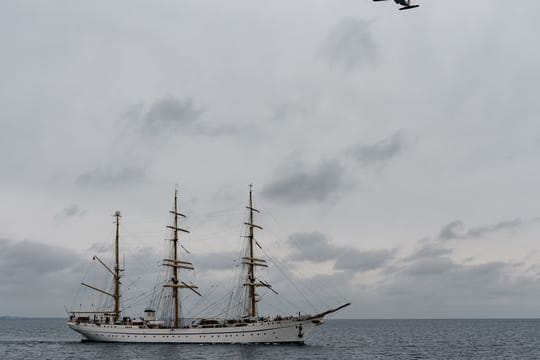 Das Segelschulschiff "Gorch Fock" fährt auf die Kieler Förde zu, während eine Transall der Bundeswehr das Schiff überfliegt.