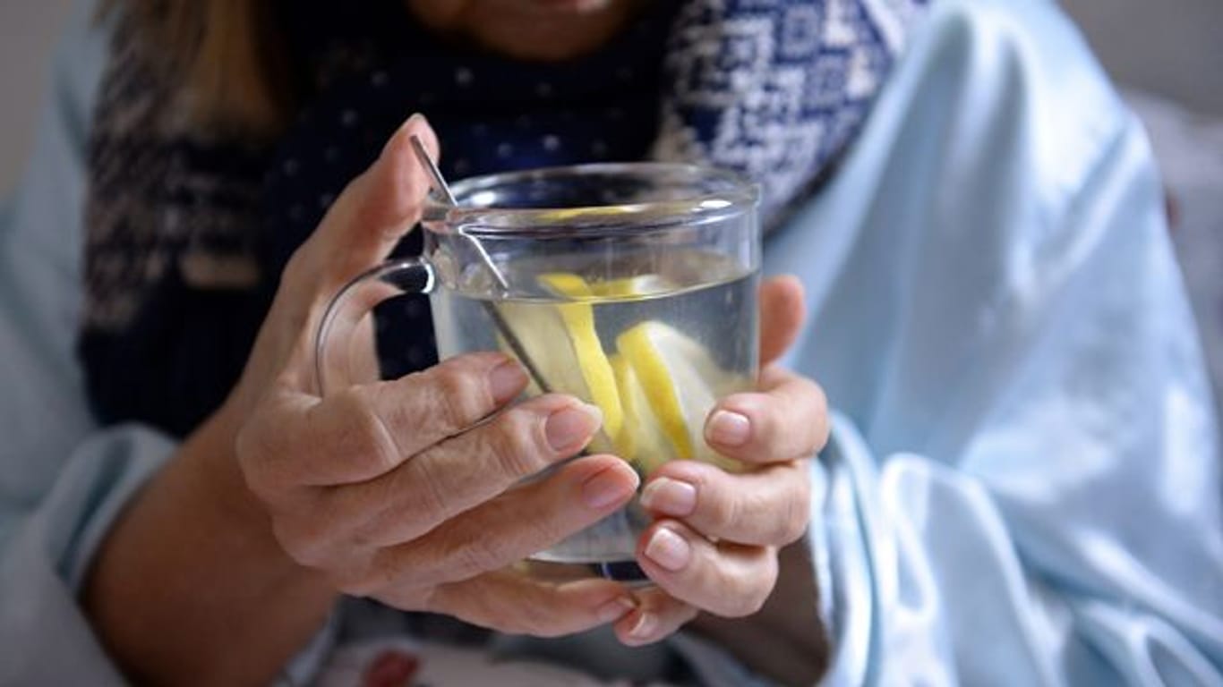 Eine Frau hält eine Tasse mit heißer Zitrone in ihren Händen.