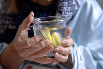 Eine Frau hält eine Tasse mit heißer Zitrone in ihren Händen.