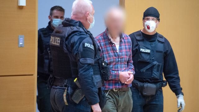 Der Angeklagte wird von einem Polizisten in den Verhandlungssaal geführt. Der Angeklagte wird von einem Polizisten in den Verhandlungssaal geführt.