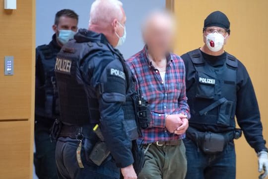 Der Angeklagte wird von einem Polizisten in den Verhandlungssaal geführt.