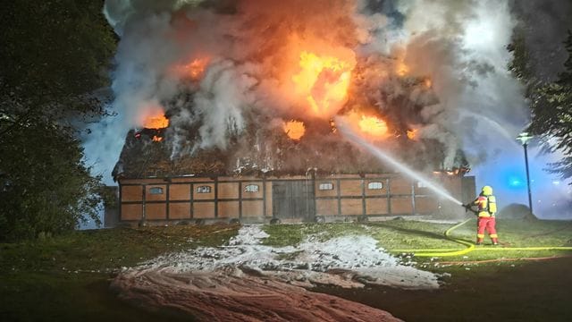 Feuerwehrleute löschen das Feuer in der mit Reet gedeckten Museumsscheune.