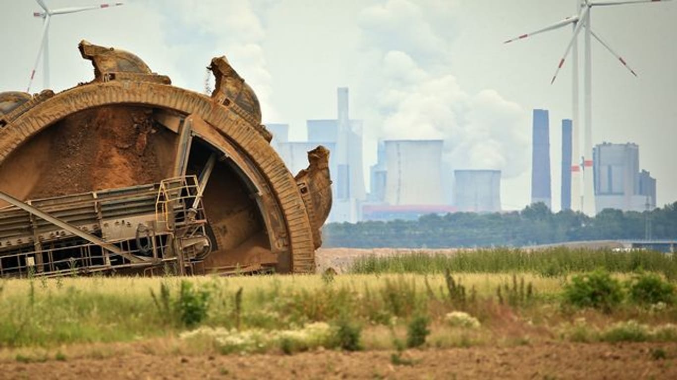 Der Schaufel eines Braunkohlebaggers baggert im Tagebau Garzeiler; im Hintergrund stehen eines der RWE-Kraftwerke und daneben Windräder.