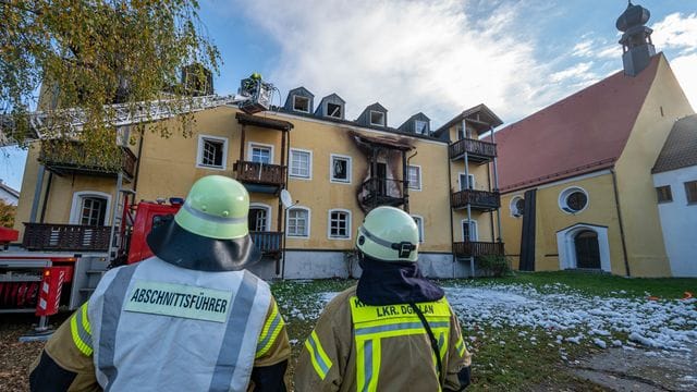 Feuerwehrmänner stehen vor einem ausgebrannten Mehrfamilienhaus.
