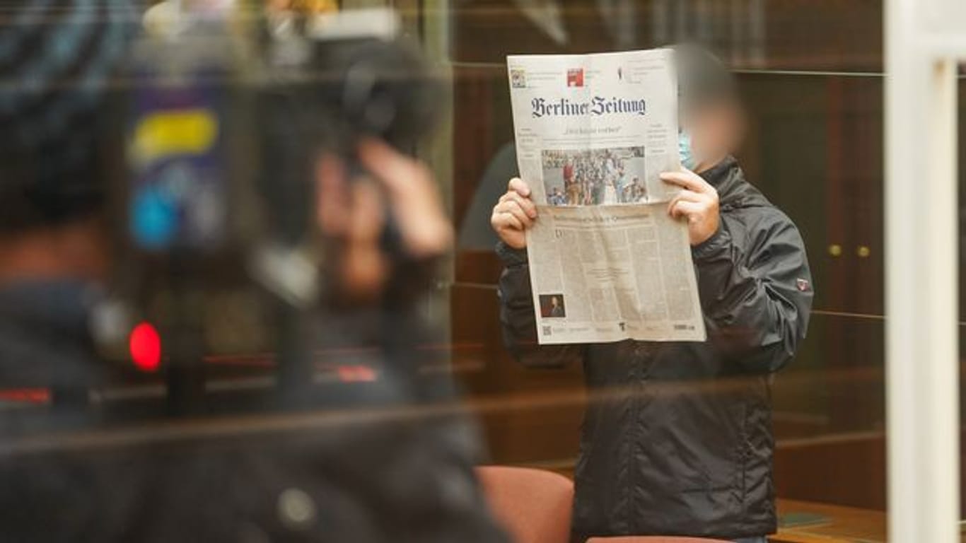 Der Angeklagte hält sich eine Zeitung vors Gesicht, während er zum Prozessbeginn in den Gerichtssaal im Berliner Kammergericht kommt.