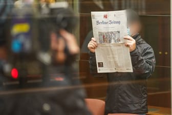 Der Angeklagte hält sich eine Zeitung vors Gesicht, während er zum Prozessbeginn in den Gerichtssaal im Berliner Kammergericht kommt.