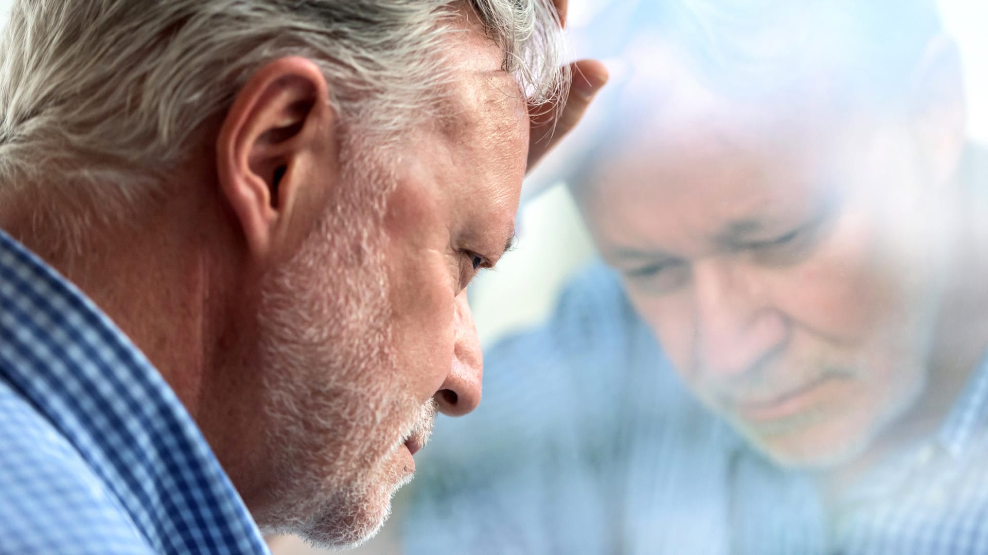 Ein nachdenklich wirkender Mann lehnt den Kopf an eine Fensterscheibe. Menschen mit Diabetes mellitus haben ein erhöhtes Risiko für psychische Erkrankungen, darunter auch Depressionen.