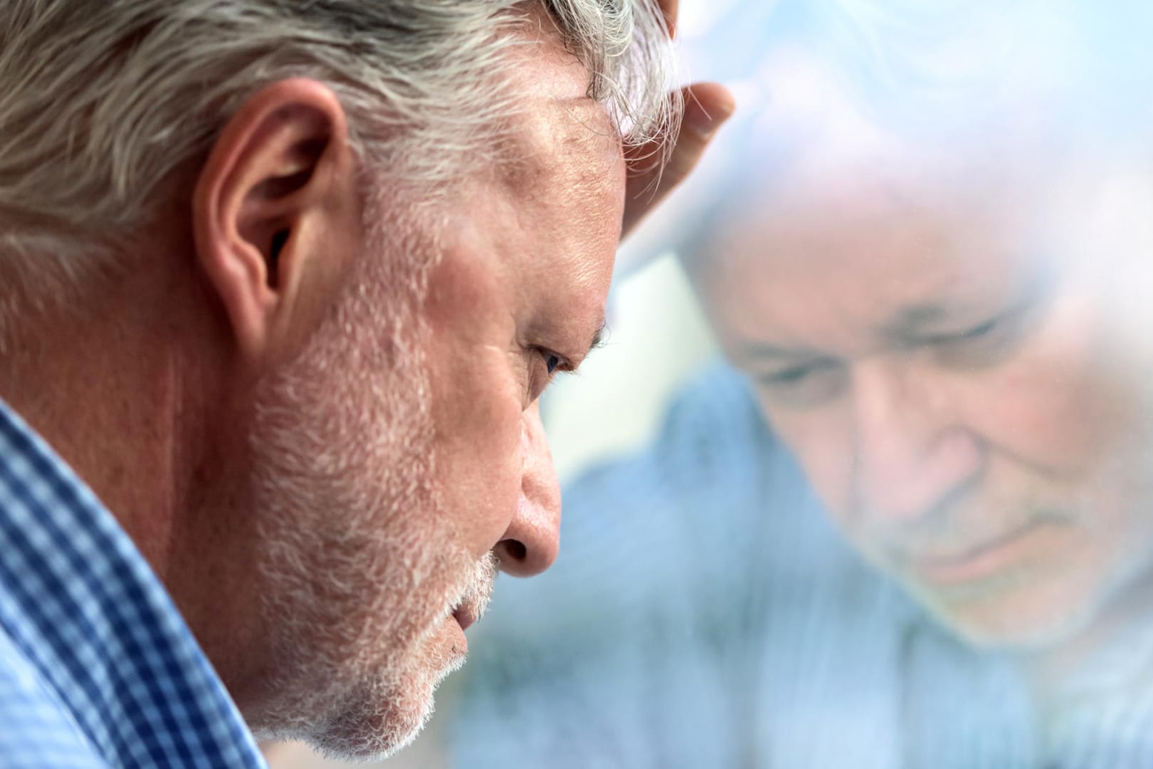 Ein nachdenklich wirkender Mann lehnt den Kopf an eine Fensterscheibe. Menschen mit Diabetes mellitus haben ein erhöhtes Risiko für psychische Erkrankungen, darunter auch Depressionen.