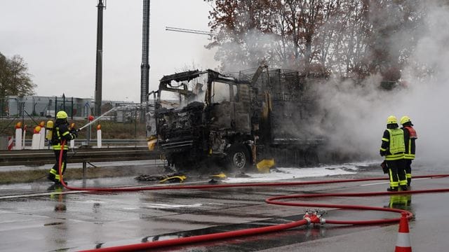 Feuerwehrleute löschen einen ausgebrannten Lastwagen: Auch die Fahrbahn wurde stark beschädigt. Feuerwehrleute löschen einen ausgebrannten Lastwagen: Auch die Fahrbahn wurde stark beschädigt.