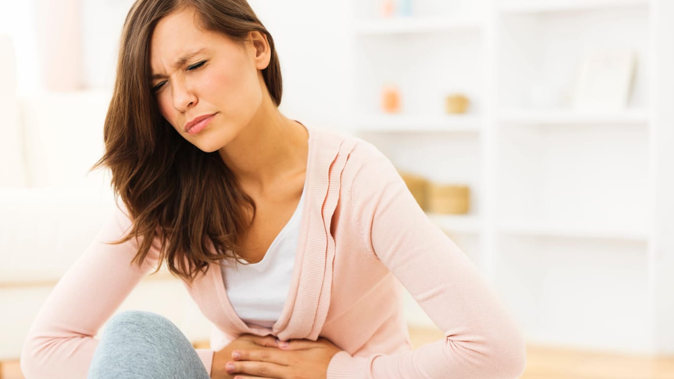 A young woman holds her stomach with her hands.  The body can react to excess iron with abdominal cramps.