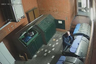 Ein Mann hält etwas in eine Mülltonne: Ein mutmaßlicher Brandstifter ist durch eine Überwachungskamera in Hamburg aufgezeichnet worden.