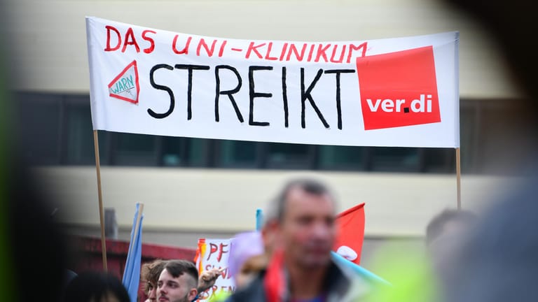 Streikende Beschäftigte halten bei einer Kundgebung ein Transparent in die Höhe (Archivbild): In den NRW-Unikliniken streiken bis zu 1.500 Personen.