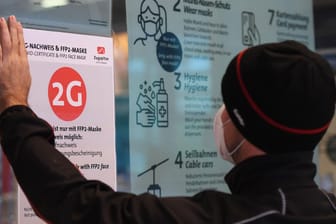 Ein Mitarbeiter einer Bergbahn in Bayern klebt die neuen 2G-Regeln an eine Eingangstür.
