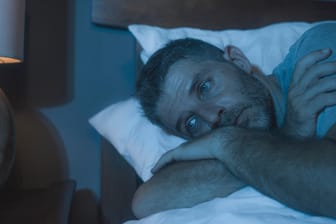 Mann liegt schlaflos im Bett: Schlafstörungen können im Alltag stark belasten.