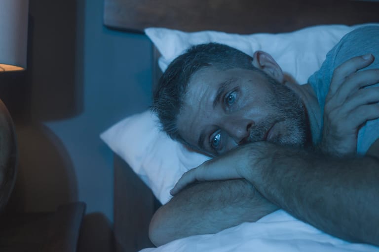 Mann liegt schlaflos im Bett: Schlafstörungen können im Alltag stark belasten.