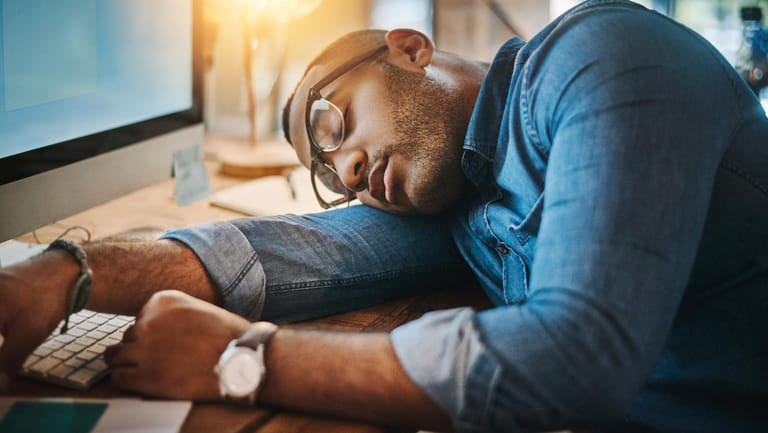 Mann ist am Schreibtisch eingenickt: Eine Schlafapnoe kann zu extremer Schläfrigkeit am Tag bis hin zum unfreiwilligen Einnicken führen.