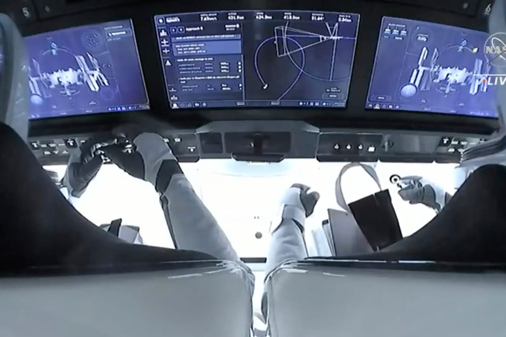 Blick aus dem Cockpit der Dragon-Kapsel: Zwei Astronauten sitzen vor den Bildschirmen beim Andockmanöver.