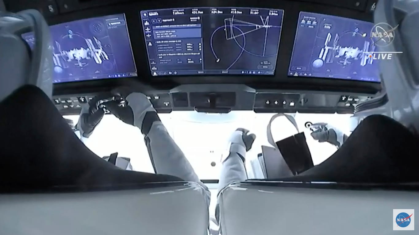Blick aus dem Cockpit der Dragon-Kapsel: Zwei Astronauten sitzen vor den Bildschirmen beim Andockmanöver.