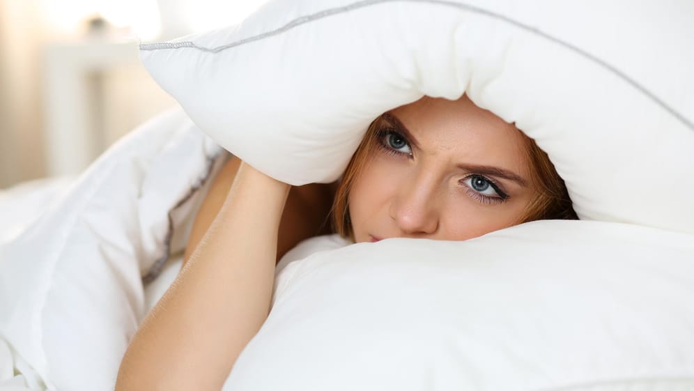 Junge Frau liegt wach im Bett. Schlafstörungen haben viele Ursachen, mitunter Stress, Druck oder sogar ernsthafte Krankheiten.