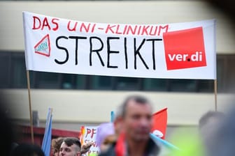 Streikende Beschäftigte halten ein Transparent mit der Aufschrift "Das Uni-Klinikum streikt" hoch. Ende November steht die dritte Verhandlungsrunde in Potsdam an.