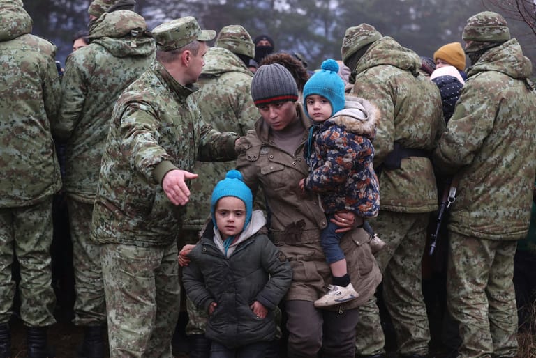 Mann mit Kindern geht an belarussischen Soldaten vorbei: Polens Grenzschutz hat den Sicherheitskräften in Belarus vorgeworfen, die an der gemeinsamen Grenze feststeckenden Migranten auf einen Durchbruch der Sperranlage vorzubereiten.