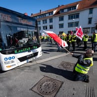 Ein Demonstrant fällt bei einem Warnstreik vor einem ankommenden Bus auf die Knie (Archivbild): Die Fahrer demonstrieren für bessere Pausenzeiten und Sonntagszuschläge.