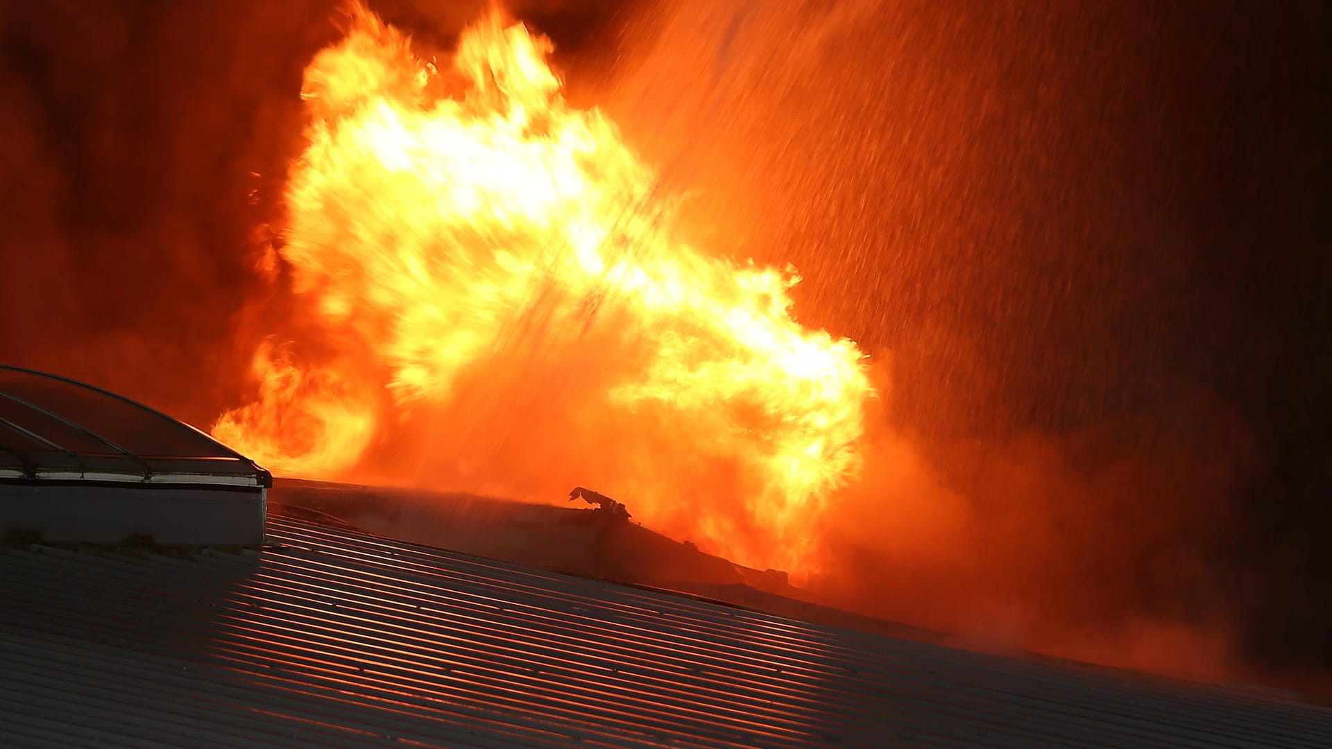 Flammen leuchten bei einem Großbrand in einer Lagerhalle in Bochum in der Dunkelheit: Der Rauch zog bis auf die Autobahn A 40.