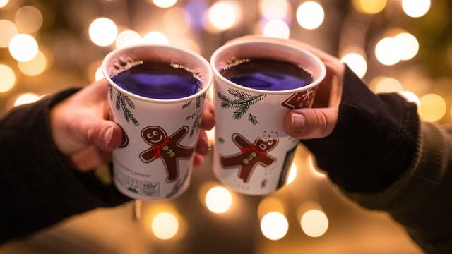 Zwei Frauen stoßen mit Glühwein in Bechern auf dem Weihnachtsmarkt an (Symbolbild): In Köln fällt der erste Weihnachtsmarkt aus.