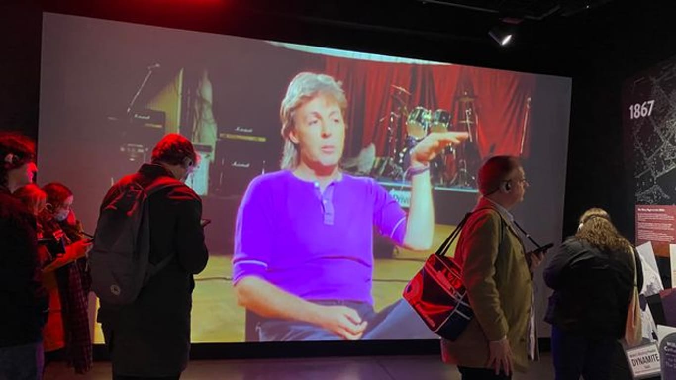 Studierende des Beatles-Studiengangs stehen in der Beatles-Installation von Strawberry Field vor einem Video von Beatles-Mitglied Paul McCartney.