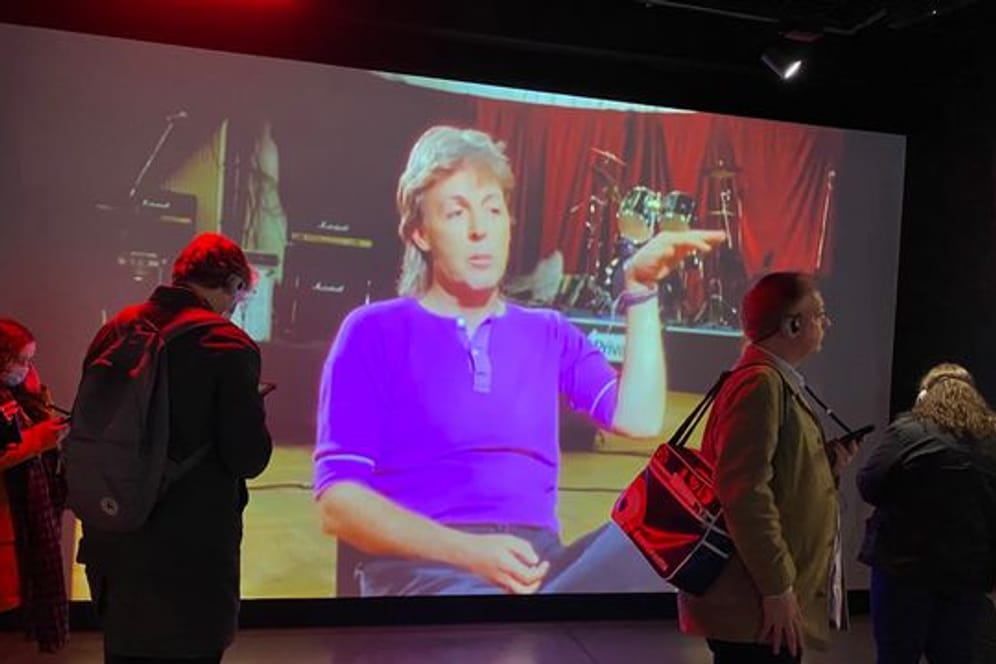 Studierende des Beatles-Studiengangs stehen in der Beatles-Installation von Strawberry Field vor einem Video von Beatles-Mitglied Paul McCartney.