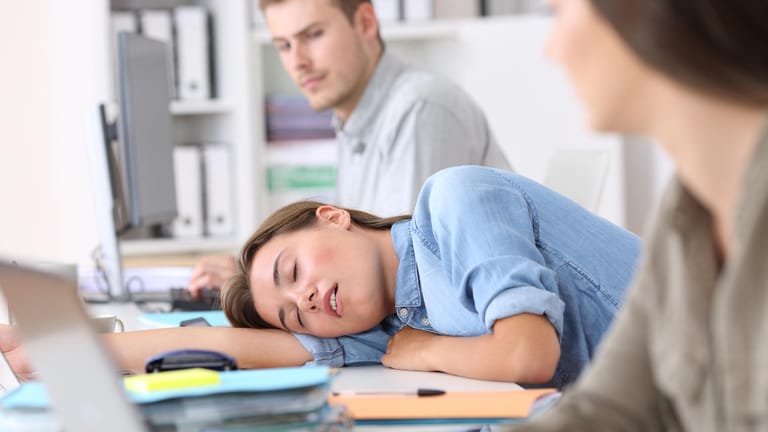 Eine junge Frau schläft am Arbeitsplatz.