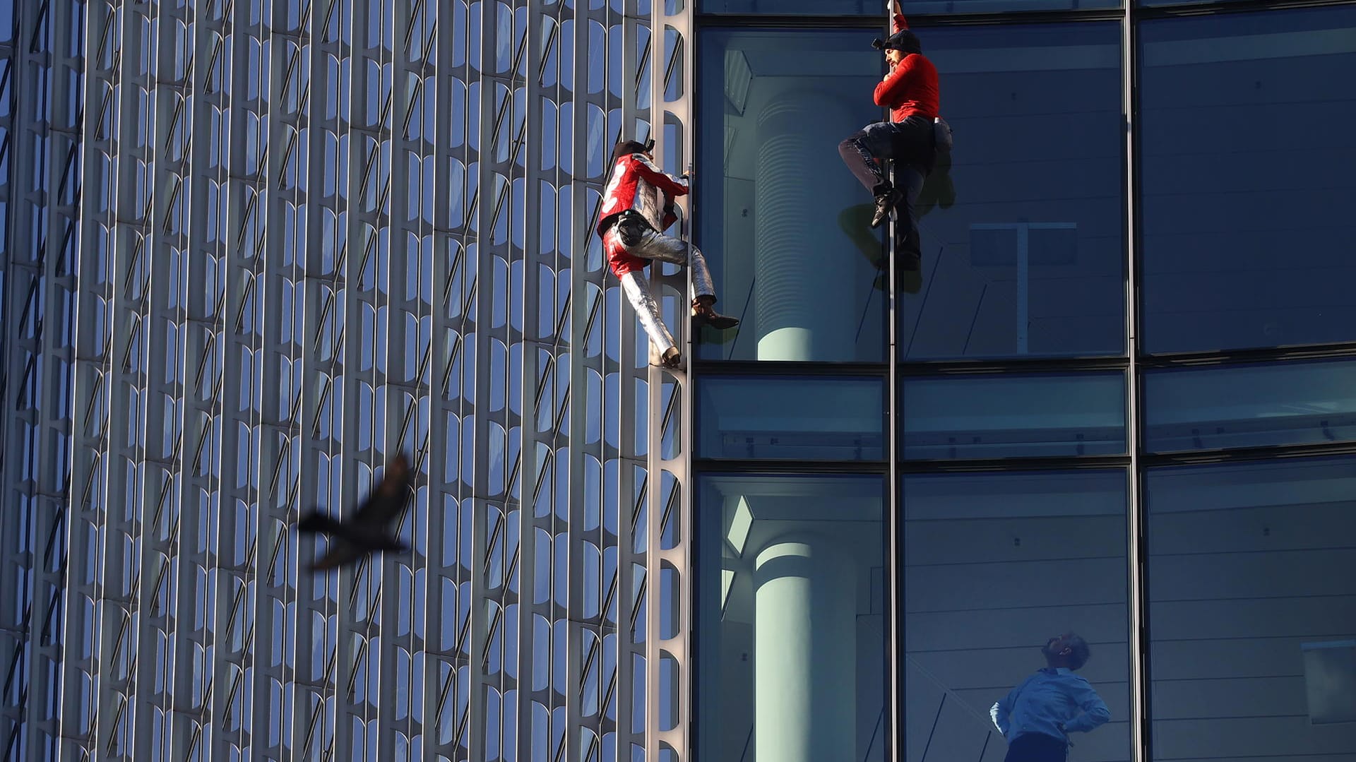 Alain Robert und Leo Urban an der Fassade: Ein Mann im Gebäude schaut ihnen erstaunt hinterher.