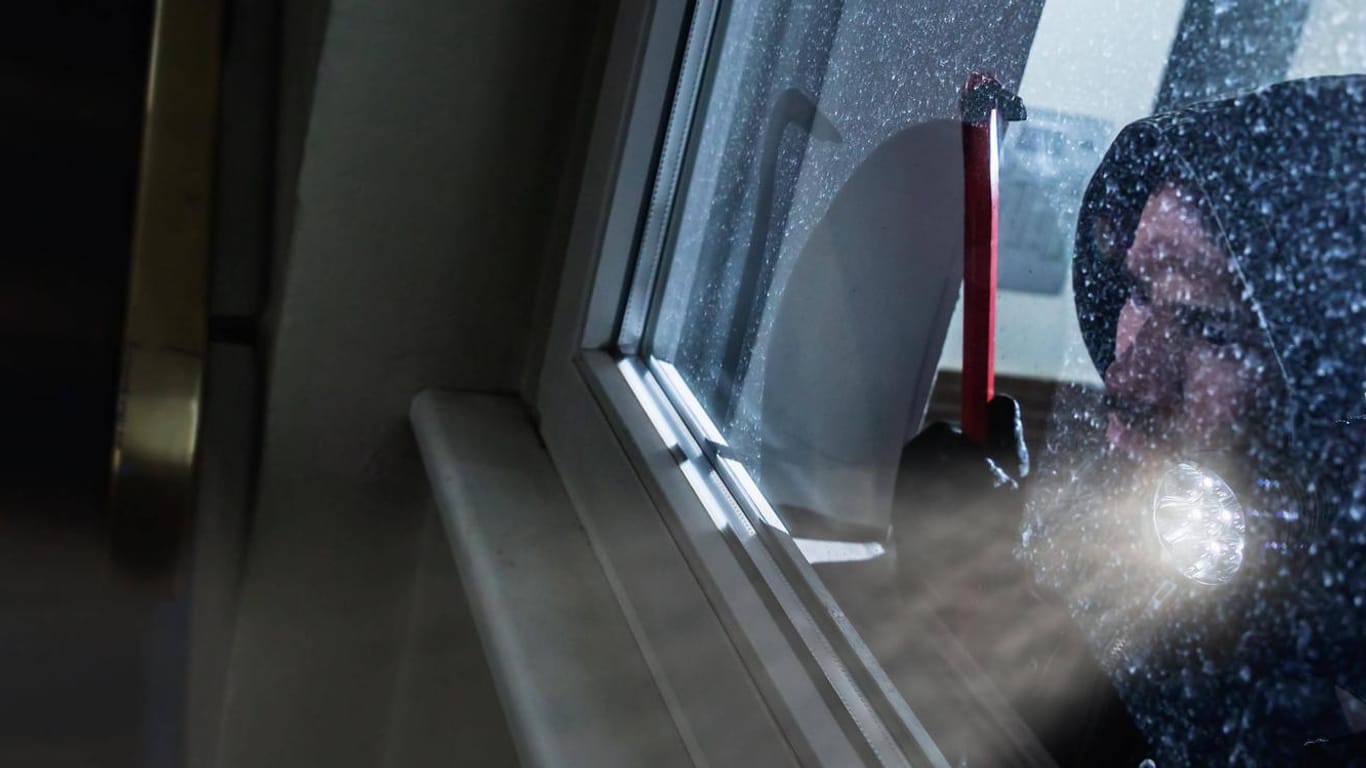 Ein Einbrecher guckt mit einer Taschenlampe durch ein Fenster (Symbolbild): Die Täter machten mehrere Zehntausend Euro Beute.