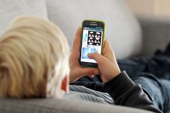 Ein Kind mit einem Handy (Symbolbild): Eine Initiative fordert die Rückkehr zu alten Lernmitteln.