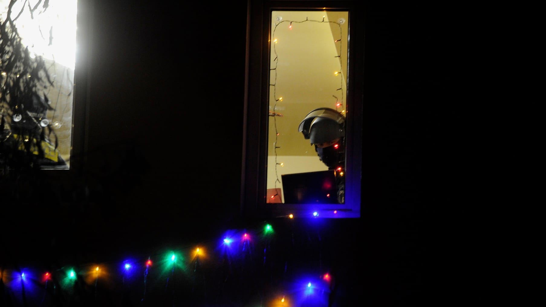 Ein Polizist mit Helm und Visier schaut aus dem Fenster einer Clan-Villa. In den frühen Morgenstunden hat hier eine Razzia begonnen, der Einsatz läuft noch.