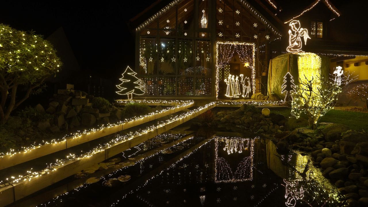 Ausgesägte Krippenfiguren, mit Lichtern umrahmt, leuchten im Garten eines sogenannten Weihnachtshauses.