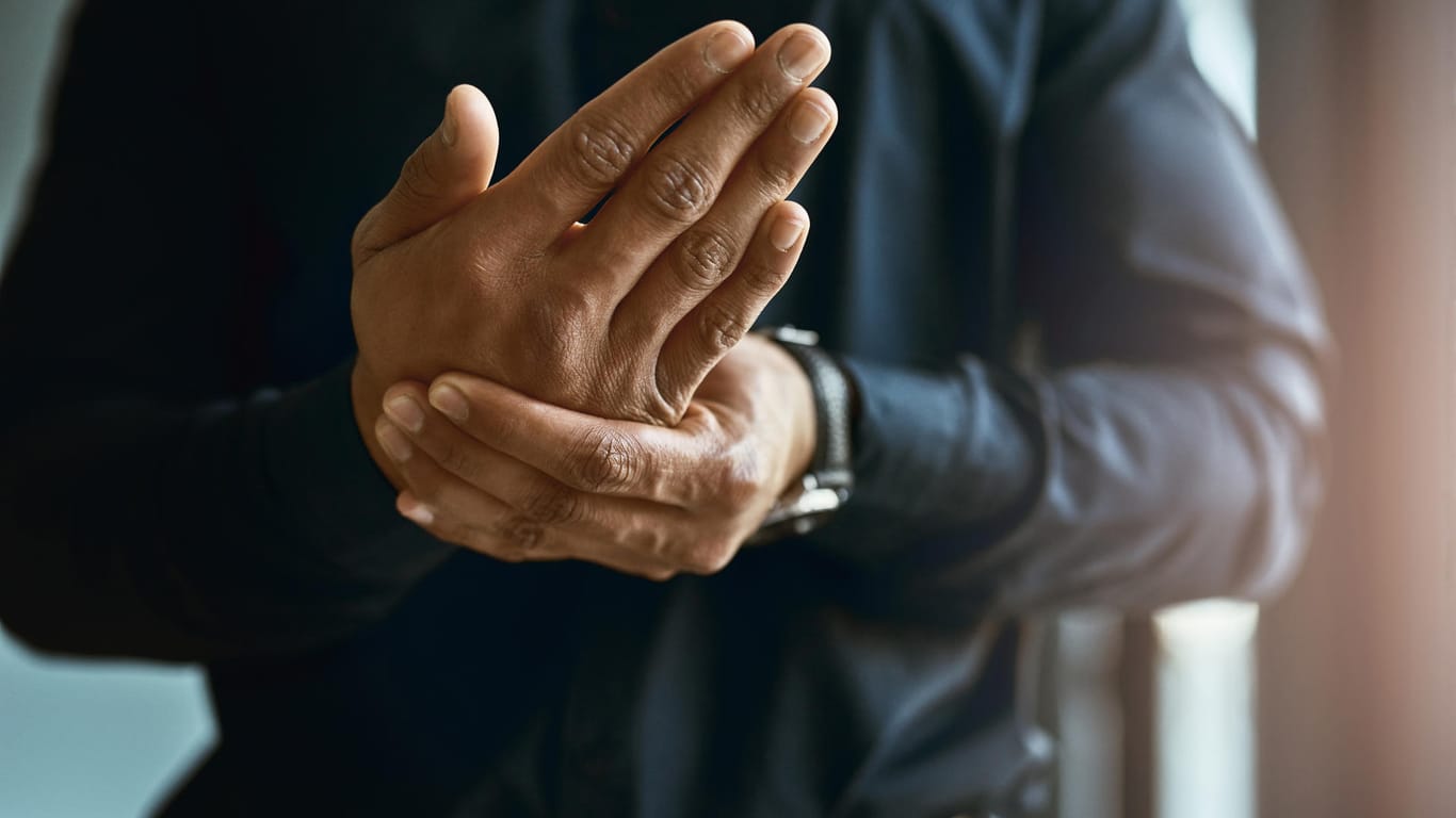 Mann massiert sich die Hand: Eine rheumatoide Arthritis beginnt oft mit Schmerzen in den Hand- oder Fingergelenken.
